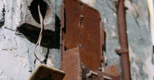 A close-up of a rusty light switch on a weathered concrete wall with exposed wires.